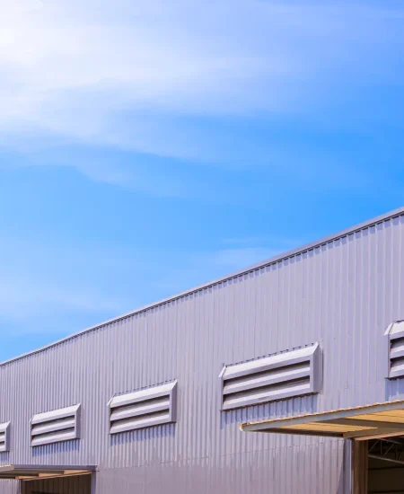 Factory warehouse building with entrance door and ventilation louver on gray aluminium corrugated steel exterior wall against blue sky background, low angle and perspective side view