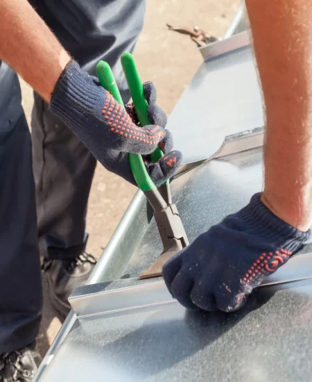 Roofer builder worker finishing folding a metal sheet using special pliers with a large flat grip