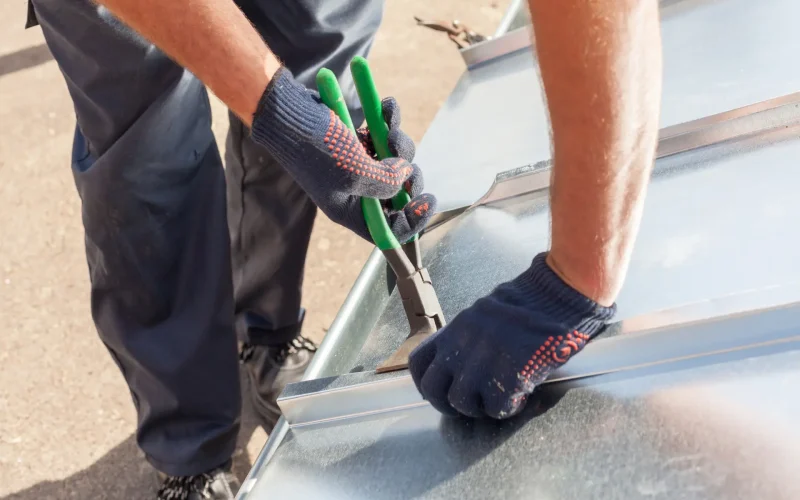 Roofer builder worker finishing folding a metal sheet using special pliers with a large flat grip